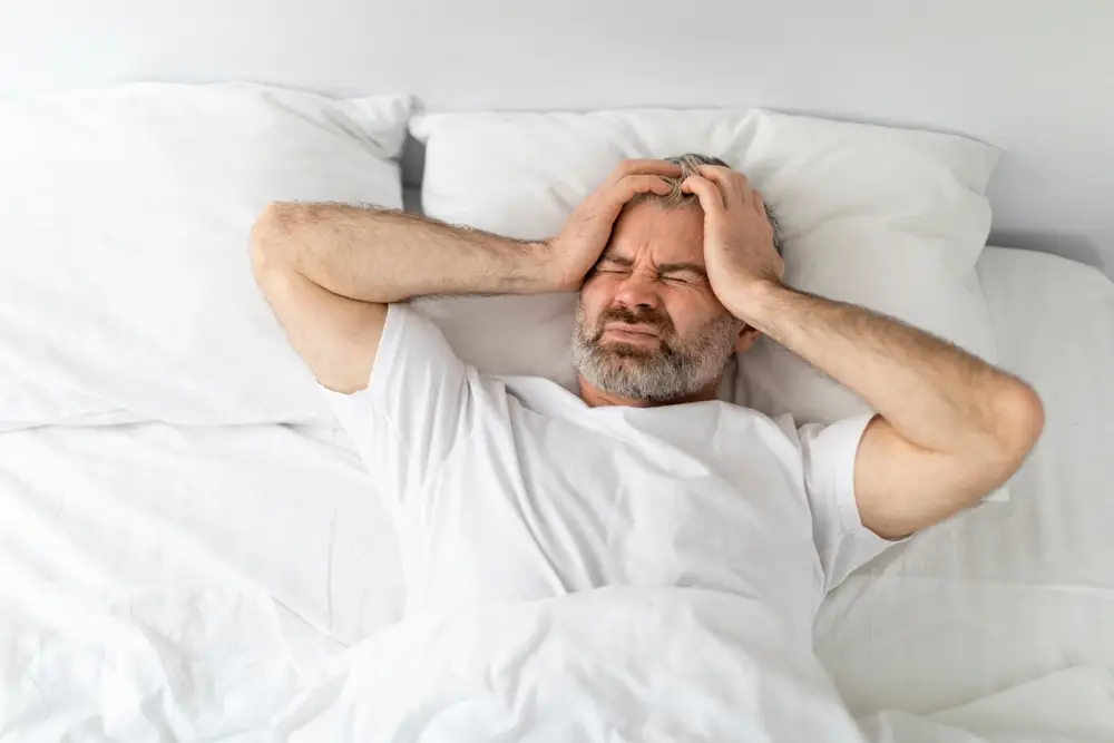 muž ležící v posteli s bolestí hlavy